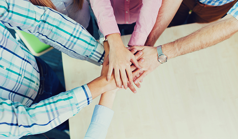 An image for a blog titled "Best Practices for Backing up Your Patient Data" showing a diverse group of professionals in an office, united, holding hands. Illustrates teamwork and collaboration.